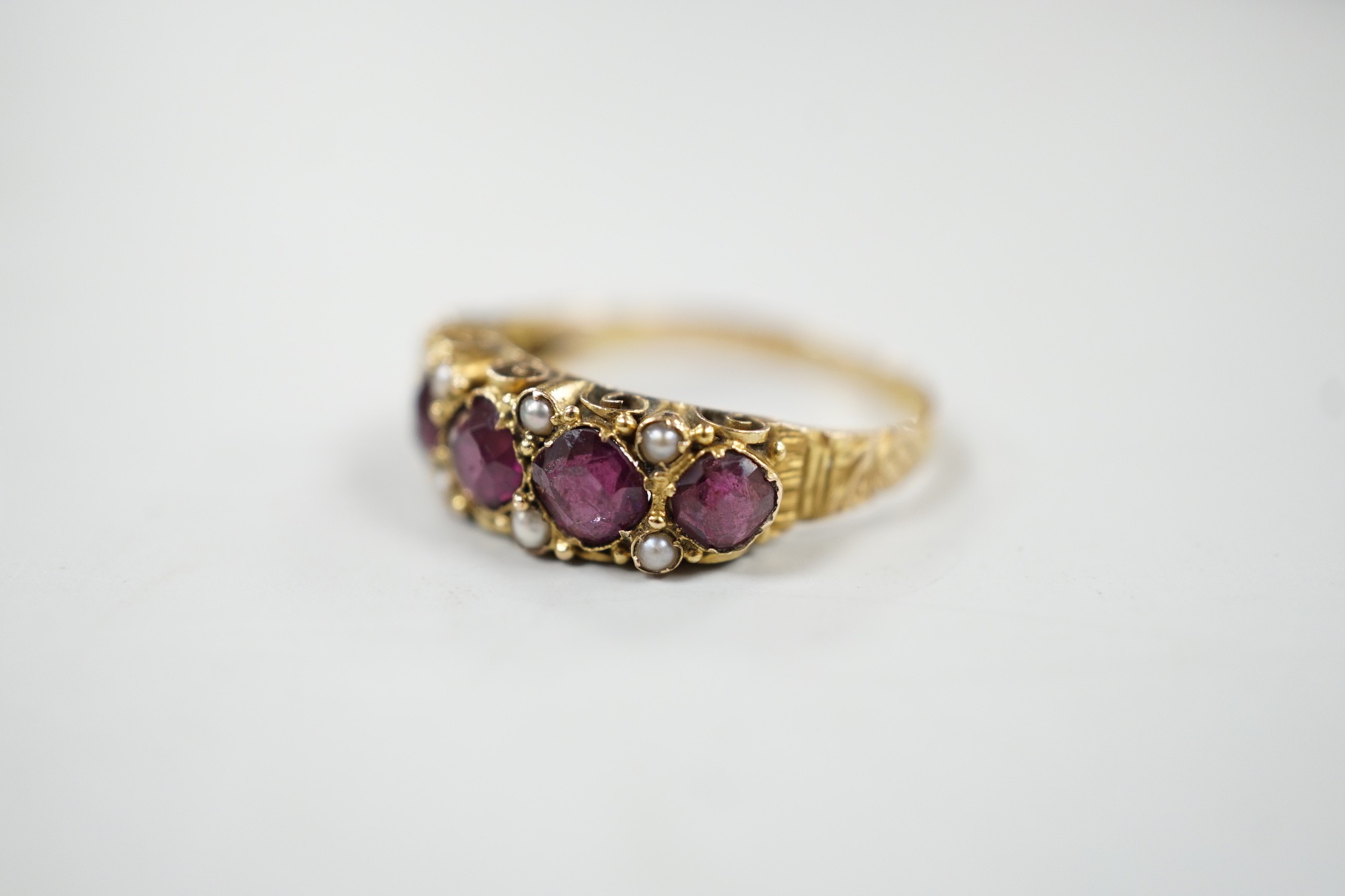 A late Victorian 15ct gold and graduated five stone garnet set half hoop ring, with split pearl spacers, size, P/Q, gross weight 2.5 grams.